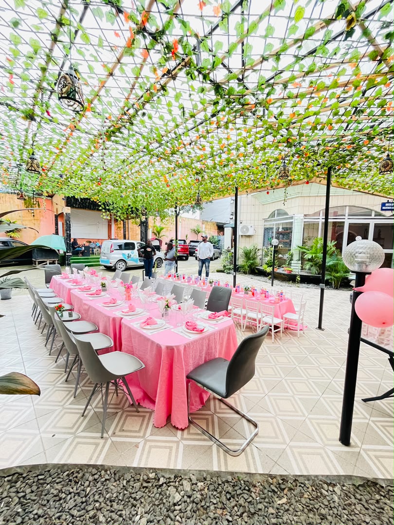Cour extérieure du restaurant dressée pour un banquet, longues tables nappées de rose sous une tonnelle de feuillage