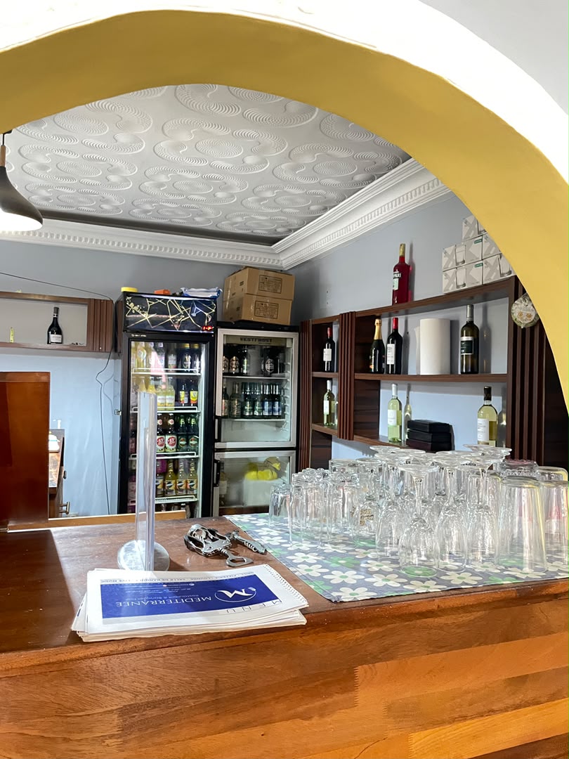 Le bar du restaurant Le Méditerranée et sa verrerie, vus à travers l'arche jaune de la salle